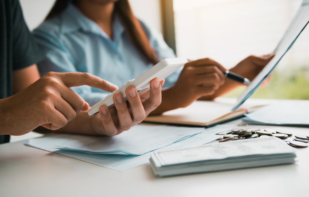 Two people reviewing documents and using a calculator to work out the cost to set up a limited company, with money and paperwork on the desk