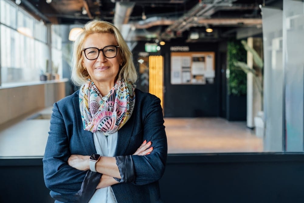 Confident woman standing with arms crossed in a modern office building, illustrating the professional appearance and role of a UK company director