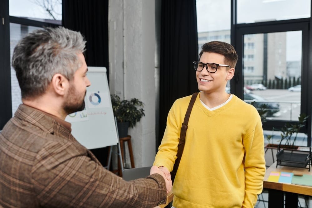 Business owner hiring first employee, shaking hands with a young professional in an office setting